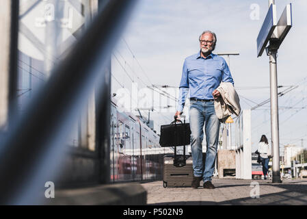 Mature businessman walking at train platform with suitcase and briefcase Stock Photo