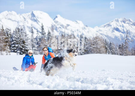 Austria, Tyrol, snowshoe hikers and dog, jumping in the snow Stock Photo