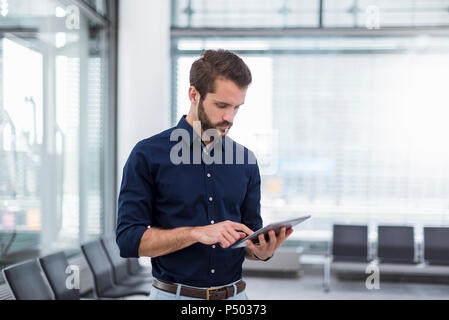 Young businessman standing in waiting area using tablet Stock Photo
