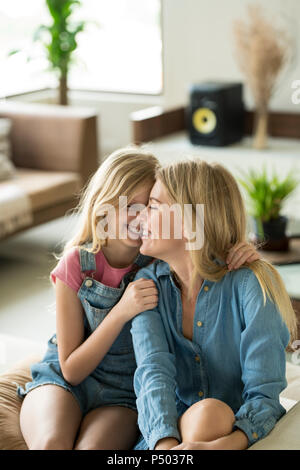 Happy mother and daughter cuddling and relaxing on a couch in a modern living room Stock Photo