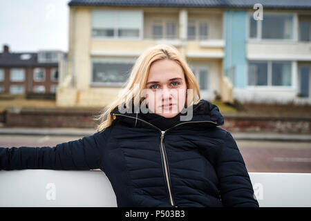 Netherlands, portrait of blond young woman sitting on bench in winter Stock Photo