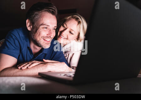 Happy couple lying on couch at home using laptop Stock Photo