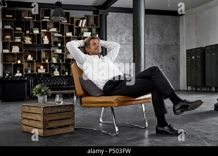 Mature man sitting on chair in loft relaxing Stock Photo