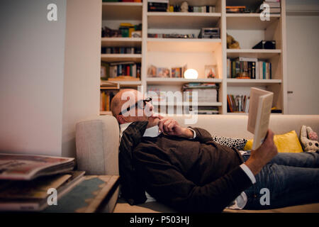 Senior man lying on couch, reading book Stock Photo