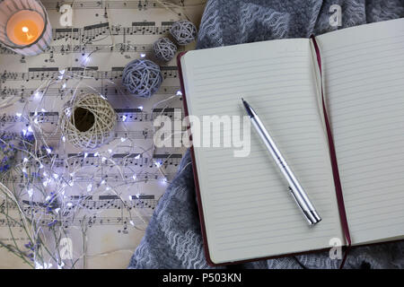 Pencil on notebook and fairy lights on music sheet Stock Photo