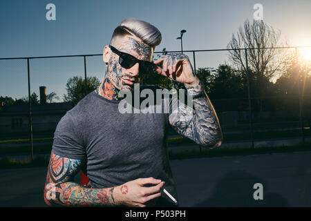 Portrait of tattooed young man wearing sunglasses smoking a cigarette Stock Photo