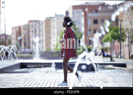 Young woman with backpack, smartphone and headphones walking in the city Stock Photo