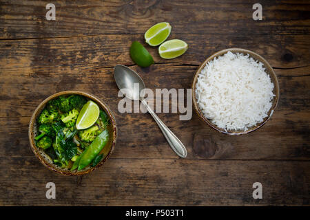 Green thai curry with broccoli, pak choi, snow peas, baby spinach, lime and bowl of rice Stock Photo