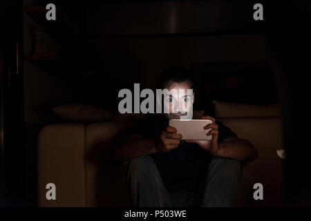 Man sitting in the dark at home starring at smartphone Stock Photo