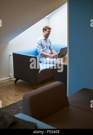 Laughing businessman sitting on couch working on laptop Stock Photo