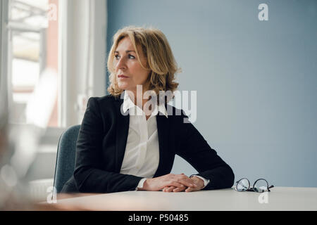 Senior businesswoman sitting at table looking sideways Stock Photo