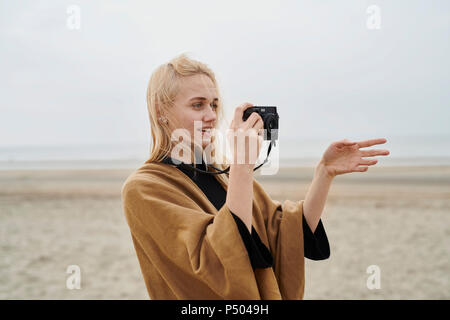 Netherlands, portrait of blond young woman with camera on the beach Stock Photo