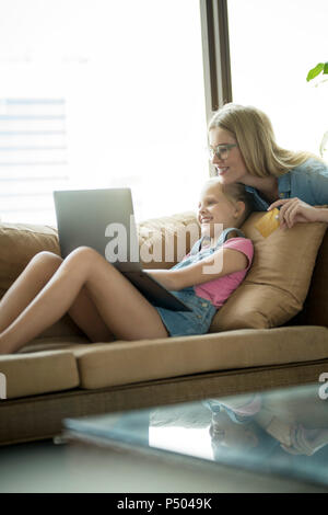 Mother and daughter in modern living room on a couch with laptop and credit card Stock Photo