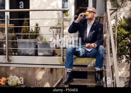 Senior man sitting on stairs of his patio, drinking coffee Stock Photo