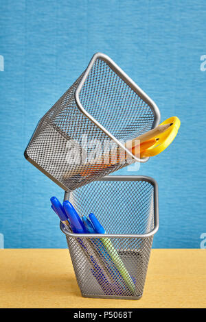Two desktop holders for writing accessories made in form of metal baskets in zero gravity on blue background. Stock Photo