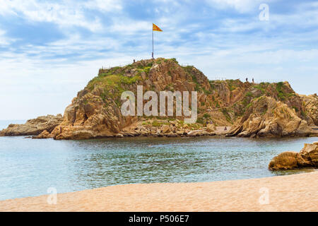 Rock Sa Palomera and sandy coast of Spanish beach resort Blanes in summertime. Costa Brava, Catalonia, Spain. Spanish flag flutters on a flagpole on t Stock Photo