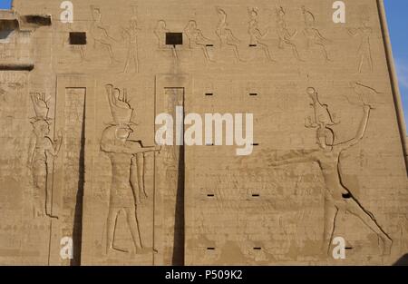 Temple of Horus. The pharaoh Ptolemy XII Neo Dionysos sacrificing prisoners to the god Horus and goddess Hahtor. Main entrance. First pylon. Detail. Edfu. Egypt. Stock Photo