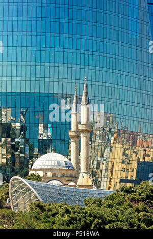 White mosque with a high minaret reflected in the glass surface of a modern skyscraper in Baku, Azerbaijan Stock Photo