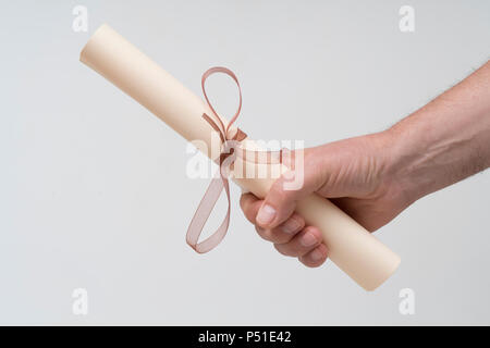 a diploma rolled up and tied with a red ribbon on the hand Stock Photo