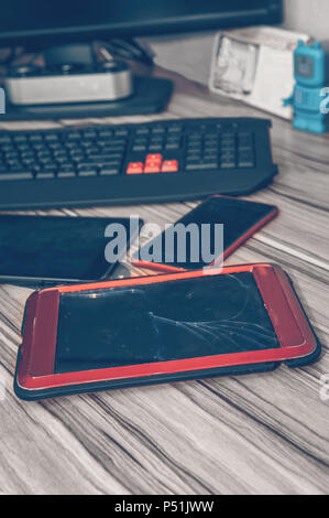 Tablet computer with broken glass, lying on the desktop with the phone and other gadgets. Screen destroyed Stock Photo