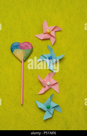 A colorful heart shape lollipop displayed with colorful pinwheels on a yellow background Stock Photo