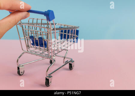 Small empty shopping cart/trolley pushed with two fingers on half pink, half blue pastel background. Minimal concept. Stock Photo