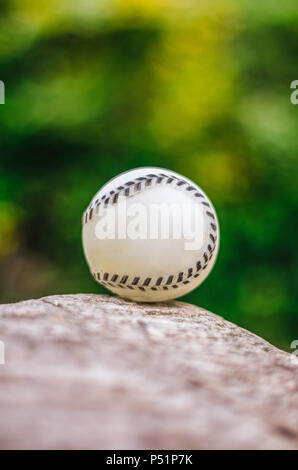 Baseball close up on rock, against green vegetation Stock Photo