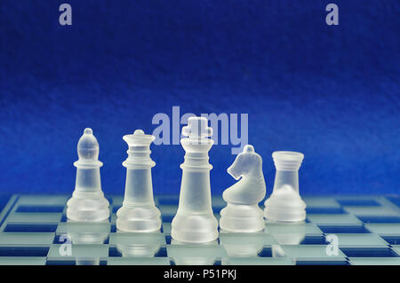 Different chess pieces displayed on a glass chessboard with a blue background Stock Photo
