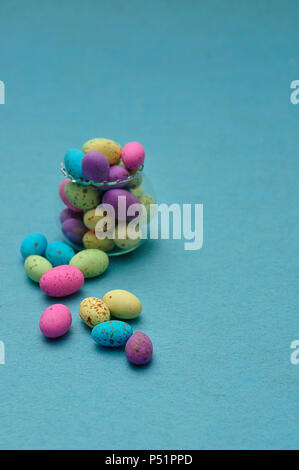 A small glass container filled with colorful speckled eggs on a blue background Stock Photo