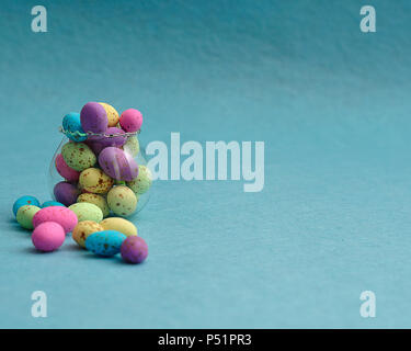 A small glass container filled with colorful speckled eggs on a blue background Stock Photo