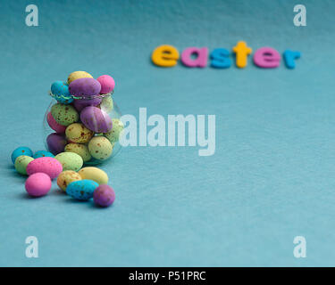 A small glass container filled with colorful speckled eggs and the word easter on a blue background Stock Photo