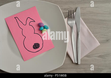 An Easter place setting with a napkin, plate, knife and fork displayed on a table with an easter bunny card Stock Photo