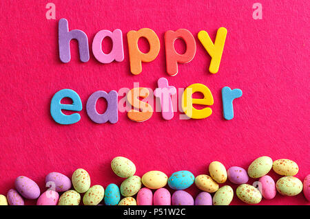 The words happy easter displayed with speckled easter candy eggs on a pink background Stock Photo