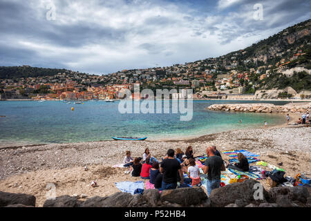 Friends having picnic on a beach in Villefranche sur Mer, resort town at Mediterranean Sea on French Riviera - Cote dAzur, France Stock Photo