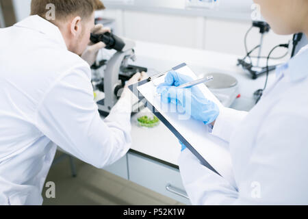 Scientists writing results of research under microscope  Stock Photo