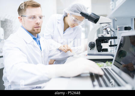 Scientist typing results of microscope research Stock Photo