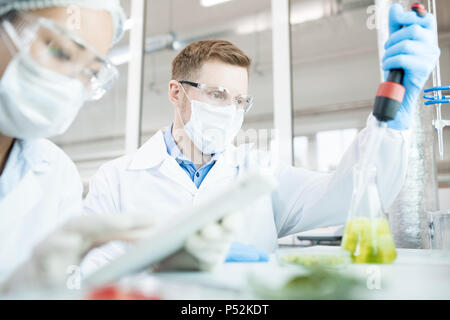 Microbiologist taking sample of solution in flask Stock Photo