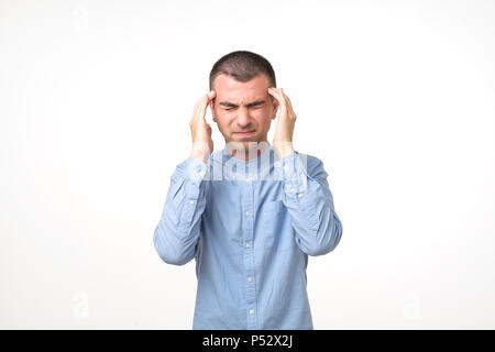 Portrait of young man in blue shirt having a headache while standing over white background. Stock Photo