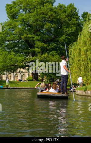 People on punt boats punting on the river Cam as people walk alongside it on a sunny Summer afternoon, Cambridge, UK