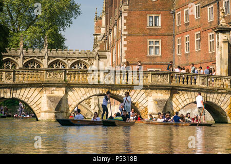 People on punt boats punting on the river Cam as people walk along a bridge by St Johns college university on a sunny Summer afternoon, Cambridge, UK