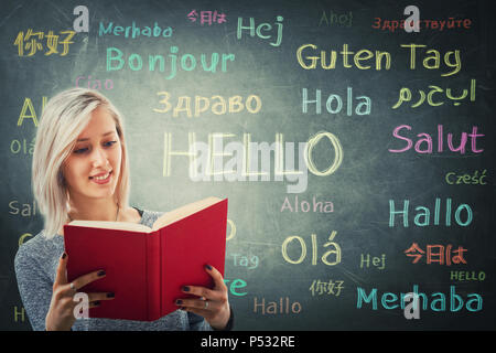 Pretty girl holding a red book in front of a huge blackboard written with the word hello in different languages and colors. Opportunity for learning m