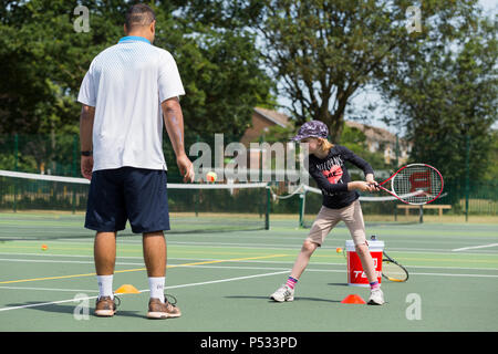 Children's tennis coaching session / lesson taking place on a full-size tennis court with kids / kids and professional tennis coach, in summer. UK. (99) Stock Photo