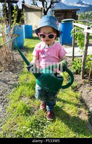 young girl carrying a large green watering can as she helps in the vegetable garden Stock Photo