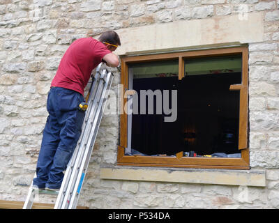 Window fitter replacing old double glazed uPVC window frames with new solid oak triple glazed window frames Stock Photo