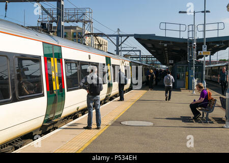 Passengers wait on a platform to board a train from Cambridge train station on a sunny Summer morning Stock Photo