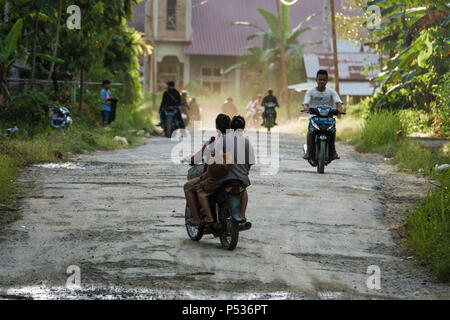 People commuting on motor scooters along potholed road in Afulu, Nias Island, Sumatra, Indonesia Stock Photo