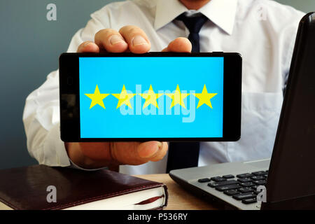 Man holding smartphone with five stars rating. Customer satisfaction. Stock Photo