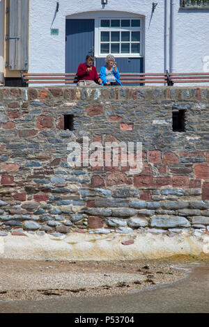 A couple enjoying an ice cream sat on a bench at the harbour at the quaint and picturesque fishing village of Cawsand in Cornwall, England, UK Stock Photo