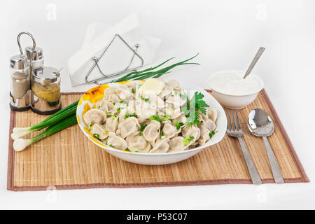 Russian dumplings with herbs and onions. Ravioli with meat. The dish is served in a plate. Served with dumplings is sour cream in a bowl. Stock Photo