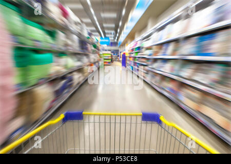 Blurred photos showcases shops on the background of a grocery cart. Long rows of racks with goods. Stock Photo